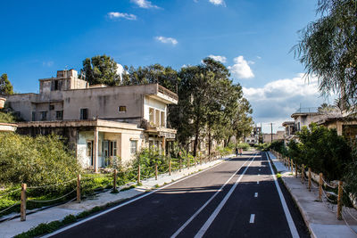 Empty road by buildings against sky