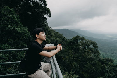 Side view of man sitting on mountain against sky