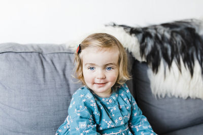 Portrait of cute girl sitting on sofa at home