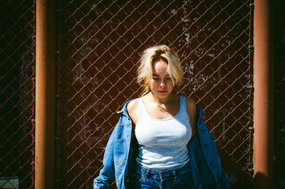 Portrait of young woman standing against fence