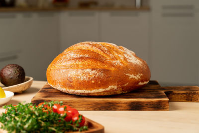 Whole loaf of freshly baked white wheat bread on wooden board on home kitchen table