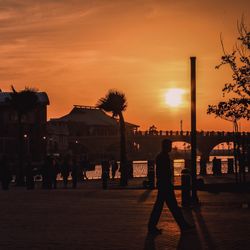 Silhouette woman walking on sidewalk in city against sky during sunset