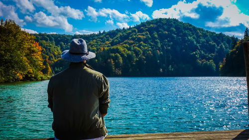 Rear view of man looking at lake against sky