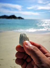 Close-up of hand holding sand at beach against sky