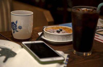 Close-up of mobile phone with drinks and pie on wooden table