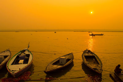 Boats moored in sea against sky during sunset