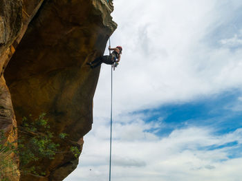 Low angle view of man climbing on rock against sky