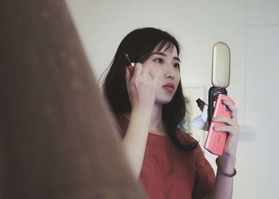 Young woman applying make-up while standing at home