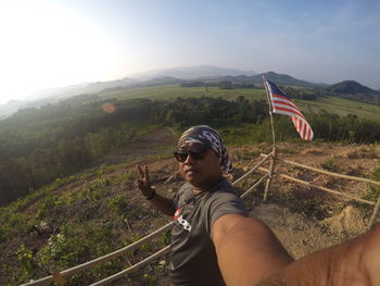 Portrait of man gesturing peace sign while standing on mountain against sky