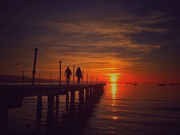 Silhouette of people on pier at sunset