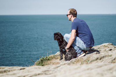 Man with dog on rock by sea against sky