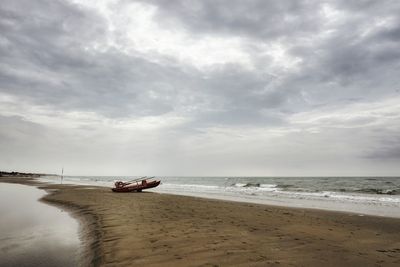 Lifeboat on sandbar against cloudy sky