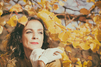 Smiling woman looking away while standing by autumn leaves