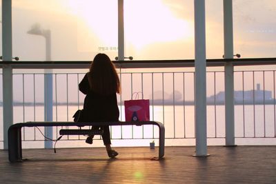 Rear view of woman sitting on chair against window