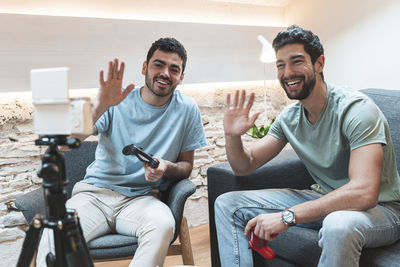 Smiling friends with video game controllers waving at camera on tripod