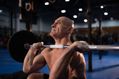 Bald senior sportsman squatting with heavy barbell