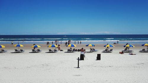 People on beach against clear blue sky