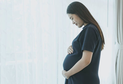 Side view of a young woman standing against wall