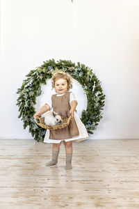 A little girl is holding a basket with a rabbit on the background of christmas decorations. new year