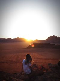 Woman sitting on land against sky during sunset