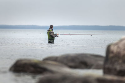 Man fishing in sea against sky