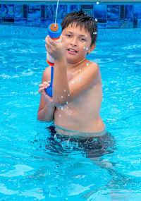 A young boy with a colorful water gun, sprays his brother as he splashes in a pool