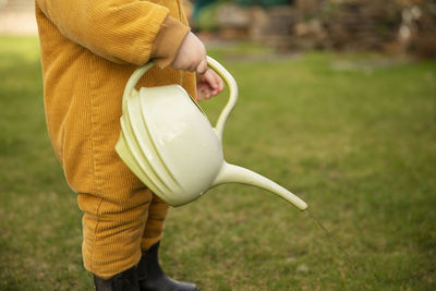 Midsection of boy holding watering can while standing on field