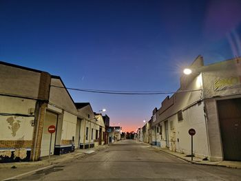 Empty road amidst buildings against clear blue sky