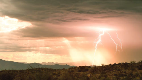 Lightning over landscape against sky during sunset