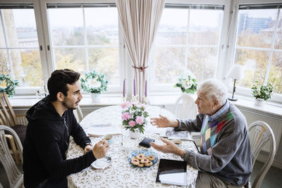 Senior man talking to caretaker at dining table in nursing home
