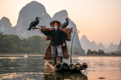 Portrait of man wearing hat standing on raft against mountain and sky