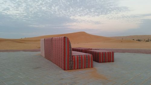 Sofa by sand dunes against sky