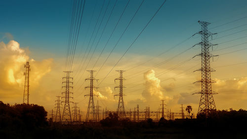 Low angle view of silhouette electricity pylon on field against sky during sunset