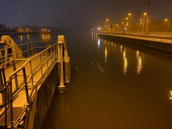 Illuminated bridge over river against sky at night