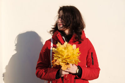 Close-up of woman with red umbrella standing against white wall