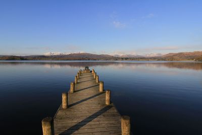 Pier on lake windermere against clear blue winter sky with snowy fells reflecting