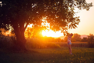 Woman standing on field against sky during sunset