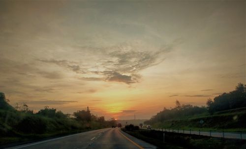 Road by trees against sky during sunset