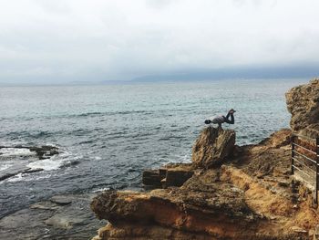 Seagull on rock by sea against sky