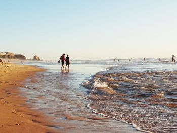 People walking on beach against clear sky