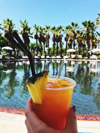 Cropped image of woman hand holding drink against swimming pool