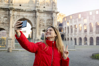 Young charming woman making a selfie in front of the colosseum during a winter vacation. 