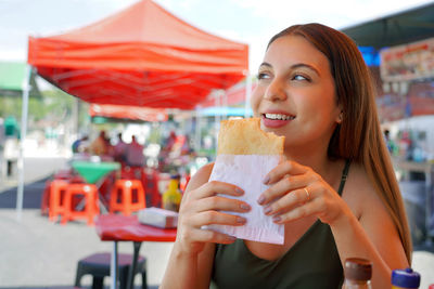 Cute brazilian girl eating pastel de feira stuffed fried pastry in sao paulo, brazil