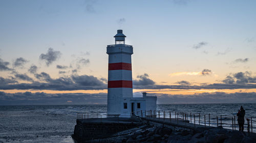 Lighthouse by sea against sky during sunset