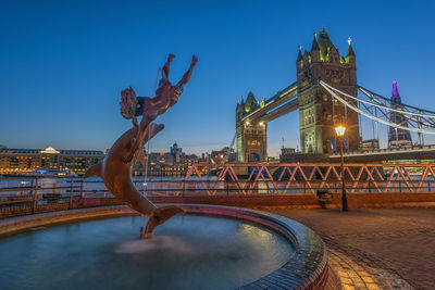 Illuminated bridge over river against sky in city