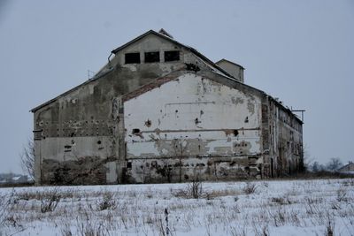 Abandoned building on field against sky during winter