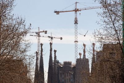 Low angle view of crane by building against sky