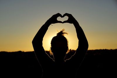 Silhouette woman showing heart shape against sky during sunset