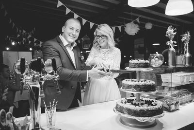 Portrait of newlywed young couple cutting cake during wedding reception