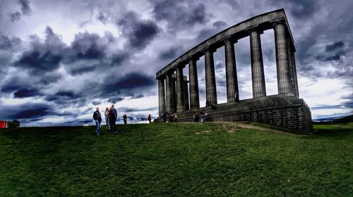 Low angle view of people on bridge against cloudy sky